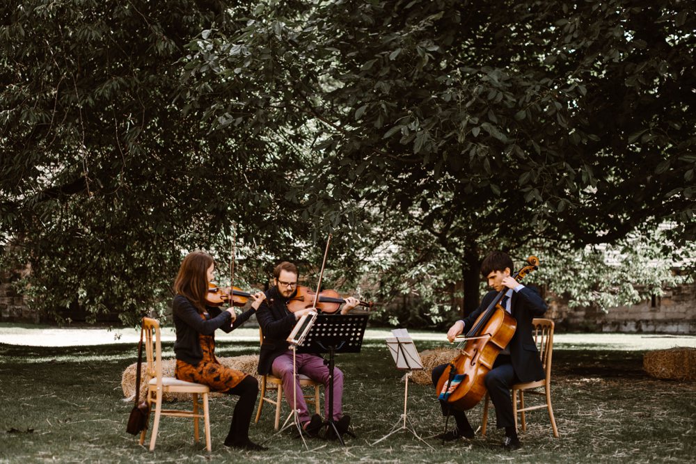 The dotted crotchets - string trio playing under the trees at rustic wedding.