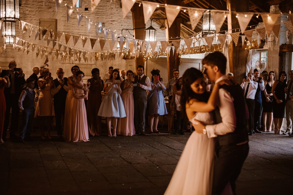 Lovely image of the couple dancing together as guests look on an rustic barm dresses with a sea of bunting