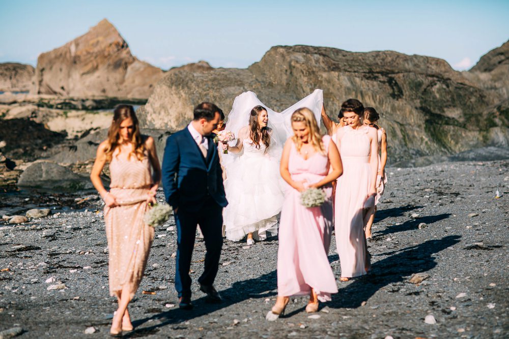 Bridemaids tip toeing over the beach pebbles